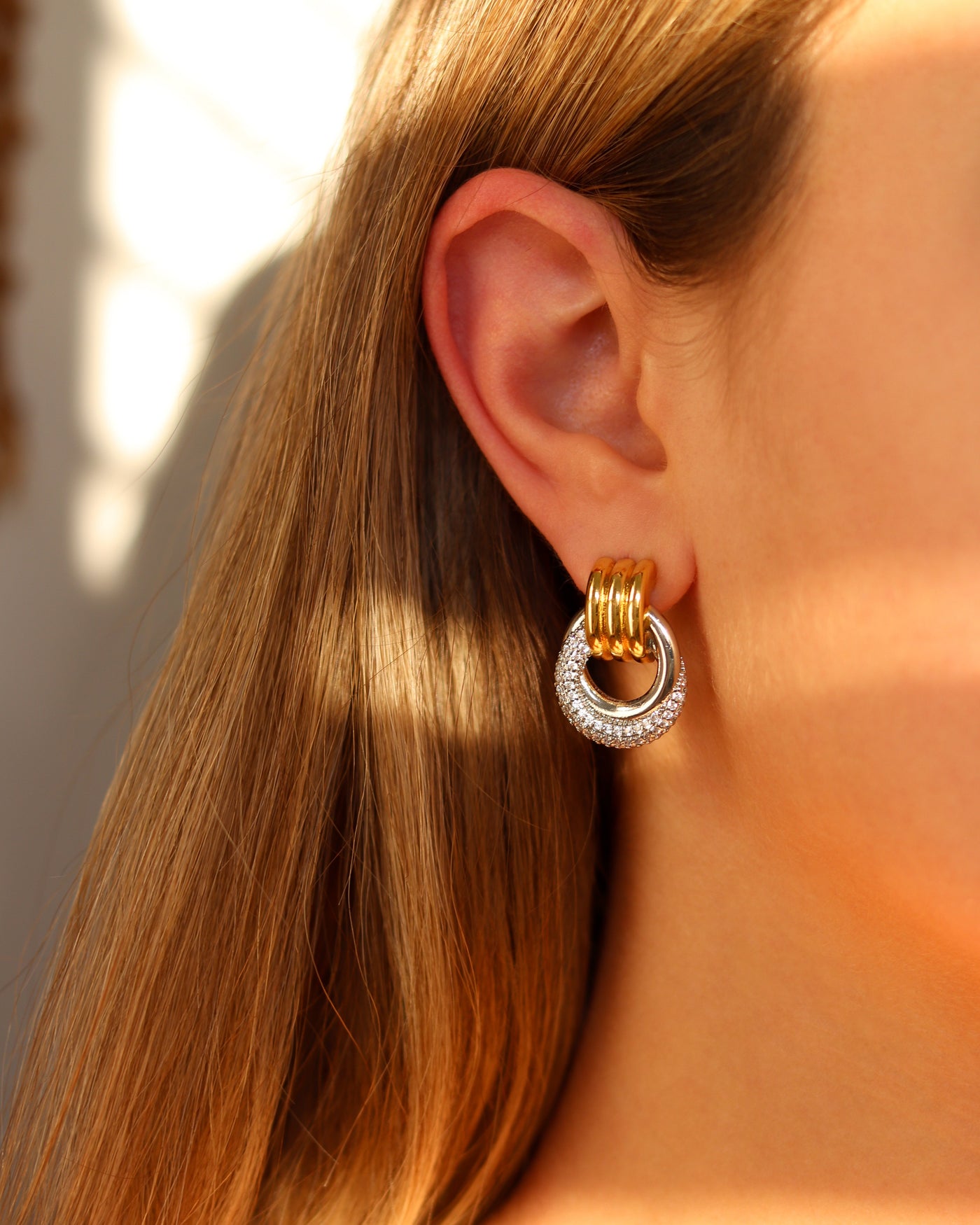 Close-up of an ear wearing gold and silver sparkly hoop earrings with a blurred background