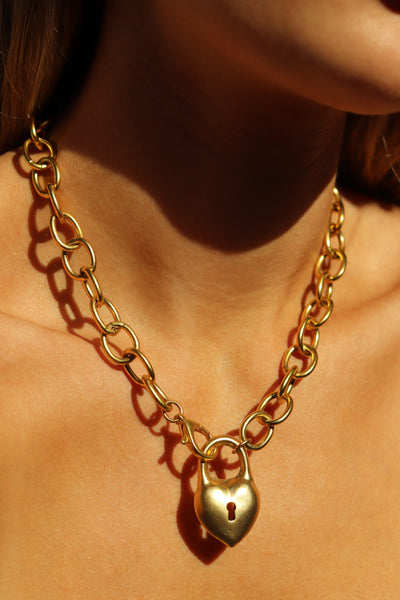 Gold chain necklace with a lock pendant on a person's neck
