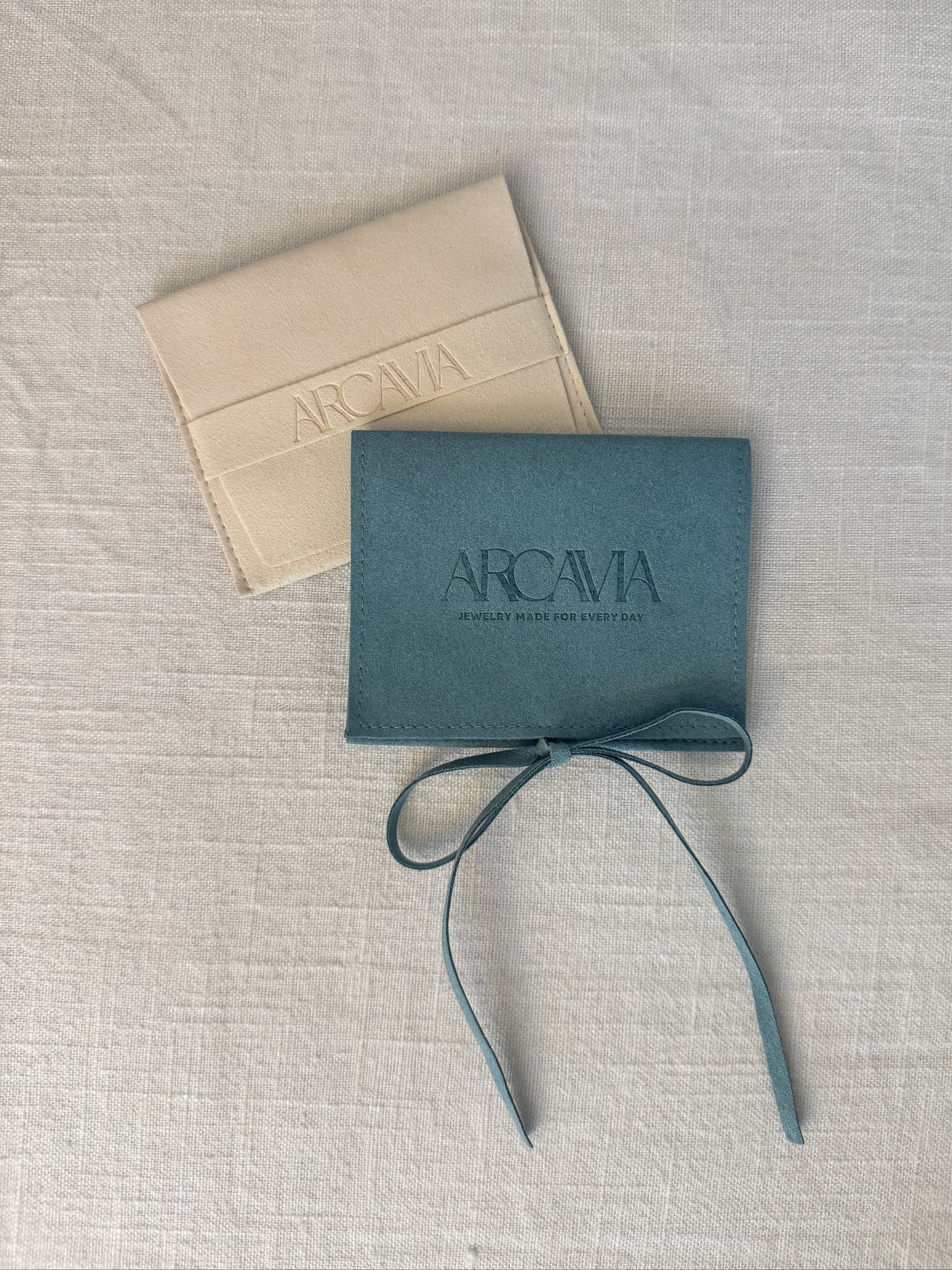 Two Arcavia boxes, one beige and one teal, on a textured surface.